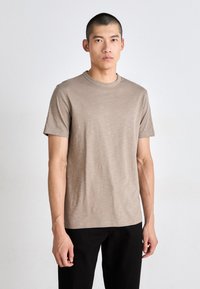 Tricou cu mânecă scurtă și gât rotund, dintr-un material bej deschis cu o textură subtilă. Are un mic logo brodat pe piept și o croială lejeră.