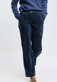 Pantalon en velours côtelé bleu marine à coupe décontractée, avec deux poches avant, une taille avec cordon de serrage et une texture douce ; associé à des chaussures à imprimé animal.