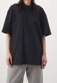 Černé oversized bavlněné tričko s krátkými rukávy a kulatým výstřihem. Nosené s volnými světle šedými kalhotami. Minimalistický design.