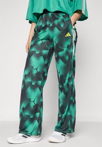 Pantalons de survêtement verts et noirs à motifs avec une taille élastique et des poches latérales. Comprend un logo Adidas jaune sur la cuisse gauche.