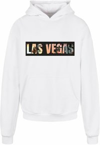 Baltas su kapu džemperis, kuriame yra juodas stačiakampis grafikas su tekstu "LAS VEGAS" ir spalvinga miesto vaizd�ų fone.