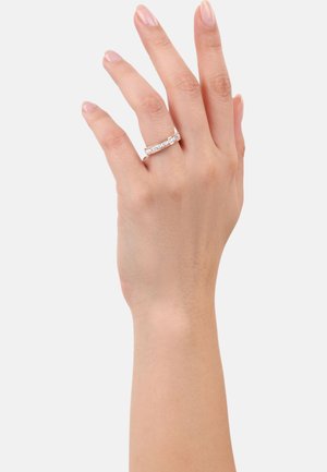 Una mano che mostra un anello d'argento brillante con una fila di piccoli diamanti, posizionata su uno sfondo bianco semplice.