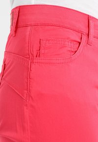 Růžové bavlněné kalhoty s zadní kapsou zdobenou šitím a designem pasu. Je patrná hladká textura a střih na míru.