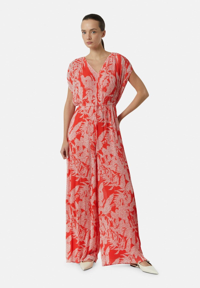 Roter und weißer Jumpsuit mit Blumenmuster, kurzen Ärmeln, V-Ausschnitt, tailliertem Bund und weitem Bein; kombiniert mit spitzen weißen Schuhen.