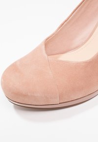 Chaussure plate à bout fermé pour femmes en daim rose doux avec bout arrondi et semelle intérieure rembourrée sur fond blanc.