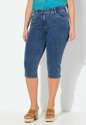 Dunkelblaue Denim-Caprihosen mit taillierter Passform, distressed Textur und umgeschlagenen Säumen, kombiniert mit sandfarbenen Plateausandalen.