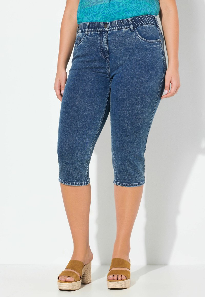 Denim capribyxor i mörkblått med en figurnär midja, slitna detaljer och upprullade benslut, tillsammans med sandaler med platå i beige.