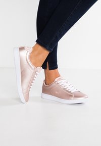 Rose gold sneakers made of smooth satin with white laces and rubber soles. Features a small logo on the side and a classic low-top design.