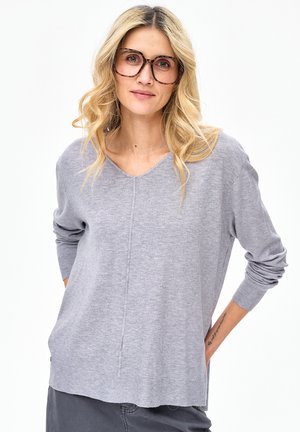 Szary sweter z dekoltem w serek o długich rękawach, z subtelnym detalem szwu i ściągaczami na mankietach. Miękka, lekka tkanina, noszony na neutralnych spodniach.