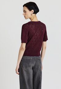 Maglione a maglia bordeaux con motivo a diamante, maniche corte e orlo cordonato, abbinato a jeans grigi a gamba larga a vita alta.