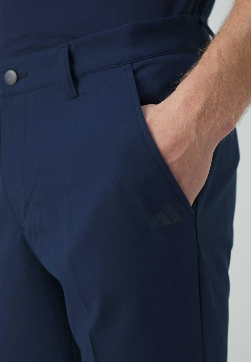 Pantalons bleu marine à la texture lisse, dotés de poches avant, d'une fermeture à bouton et d'un discret logo près de la poche.