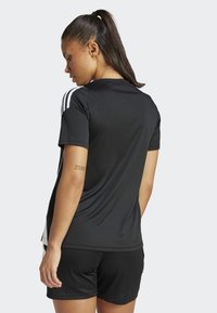 Cămașă sport neagră cu mâneci scurte, dotată cu trei dungi albe pe umeri, asortată cu pantaloni scurți negri. Textură a țesăturii netedă.