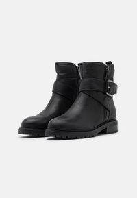 Black leather ankle boots with a round toe, side zippers, and an adjustable strap. Rubber soles with a slight heel. Textured finish details.
