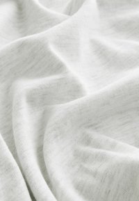 Tissu blanc doux avec des plis subtils et une texture tricotée fine, créant de douces ombres et reflets.