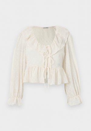 Kremowa bluzka z długim rękawem z falbanianym kołnierzykiem i mankietami, zawiązywana z przodu, z teksturowanym wzorem w kropki i dołem typu peplum.