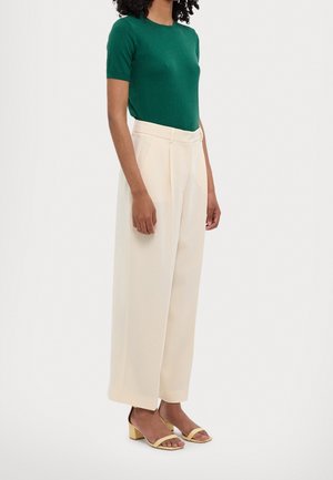 Groene top met korte mouwen, gecombineerd met high-waisted, wijde crèmekleurige broek en gele haksandalen. Soepele texturen en een eenvoudig ontwerp.