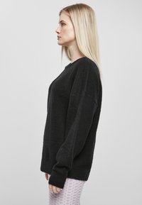 Fekete kötött pulóver texturált felülettel és oversized ujjakkal, kerek nyakkivágással. Puha anyag elér a csuklóig.