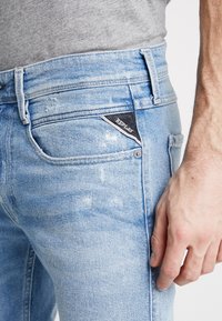 Ljust blå denimjeans med en slim fit. Har slitna detaljer och en svart triangel-logotyp på bakfickan.