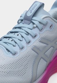 Ανοιχτό μπλε παπούτσι για τρέξιμο Asics με λεπτομερείς κορδόνια, άνω μέρος από δίχτυ και ροζ σόλα ορατή σε λευκό φόντο.
