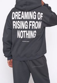 Antracytowa bluza z kapturem i dużym białym napisem na plecach "DREAMING OF RISING FROM NOTHING", w komplecie z dopasowanymi spodniami dresowymi.