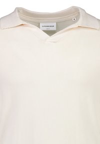 Krämfärgad, slim-fit stickad polo skjorta med v-ringning och mjuk krage. Har en etikett vid kragen med varumärkesnamn och storlek.