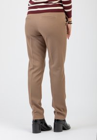 Pantaloni beige su misura con tasche posteriori, texture liscia e vestibilità slim, abbinati a stivali neri con tacco. Design semplice ed elegante.