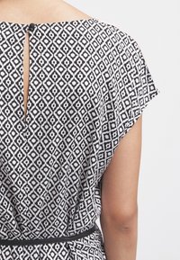 Svart och vitt mönstrat plagg med en geometrisk design. Har en nyckelhålsöppning bak och ett svart bälte vid midjan.