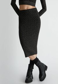 Gonna a matita nera in maglia con un motivo geometrico, abbinata a stivaletti neri con lacci e suola chunky con accenti testurizzati.