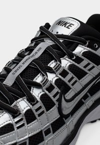 Κοντινή λήψη μαύρου και ασημί αθλητικού παπουτσιού Nike με λεπτομερείς μαύρες κορδόνια και κείμενο «MII BOWERMAN SERIES» στην ετικέτα στη γλώσσα.