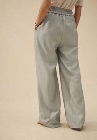 Light gray, wide-legged trousers with a pinstripe pattern, elastic waistband, and side pockets; smooth texture with a relaxed fit.