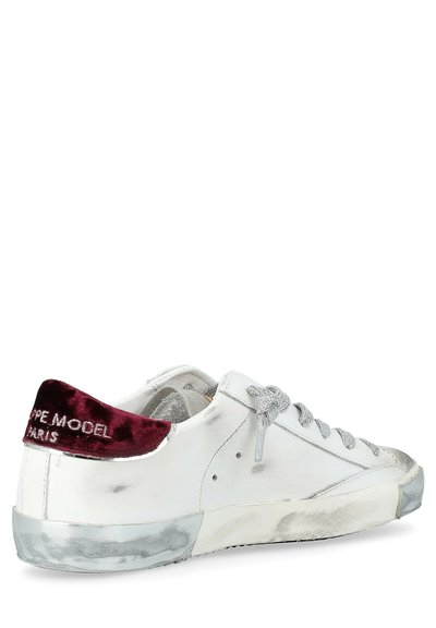 Sneaker bianca in pelle con dettagli argento, lacci grigi testurizzati e una toppa in velluto bordeaux sul retro con logo bianco. Dettagli scuri sulla suola argento.