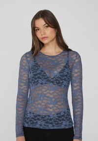 Blaues Spitzenoberteil mit langen Ärmeln, das florale Muster, durchsichtigen Stoff, einen runden Ausschnitt und eine enganliegende Passform aufweist. Es hat einen mehrlagigen Look auf einem schwarzen Hintergrund.