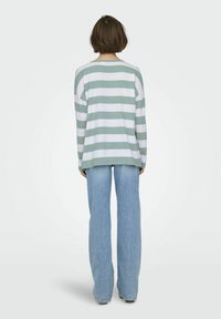 Pull long à rayures vert menthe et blanches, coupe décontractée, avec un col rond. Associé à un jean évasé bleu clair.
