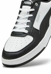 Mustvalge Puma tennisejalanõu, millel on tekstuuriga nahk ülemine, perforatsioonidega varbakast ja valged paelad. Külgedel on peened logo aktsendid.