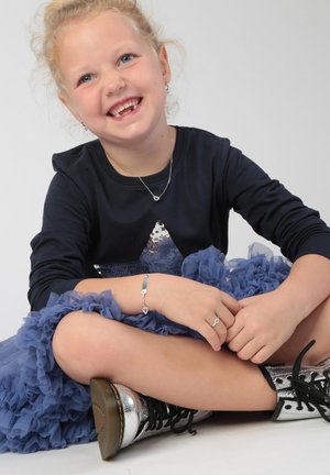 Marineblauw shirt met lange mouwen en een paillettenster, gelaagde blauwe tule rok, zilveren sieraden en metallic zwarte veterschoenen tot de enkels.