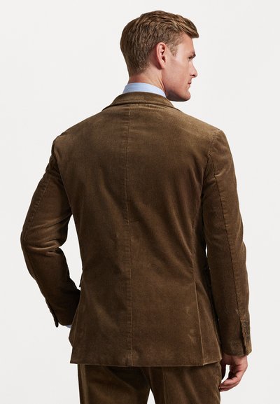 Blazer en velours côtelé marron avec une surface texturée, une fente simple et des poignets boutonnés. Il présente une coupe ajustée et des épaules légèrement structurées.