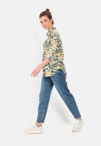 Blomstret skjorte med knapper i grøn, orange og gul, parret med lyseblå denimjeans og hvide sneakers. Slim-fit design med opkrøllede ærmer.