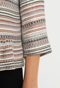 Halflange top met een gebreid patroon in wit, bruin, zwart en grijs. Heeft een textuurstof met opengeweven structuur.