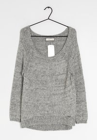 Szary sweter dzianinowy z szerokim dekoltem, długimi rękawami i nieco dłuższym tyłem. Posiada metkę zwisającą z okolicy szyi.