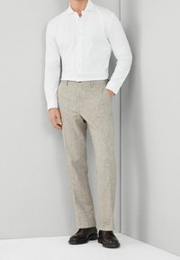 White long-sleeve button-up shirt paired with beige textured trousers and dark shoes. The outfit has a clean, tailored fit.