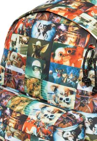 Kleurrijke rugzak van stof met een collage van Gremlin-personages, die een verscheidenheid aan uitdrukkingen en scènes in kleine vierkantjes laten zien.