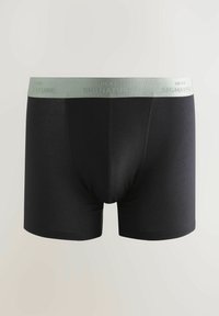 Schwarze Boxershorts aus weichem Stoff. Mit einem hellgrünen Bund, auf dem "NEXT SIGNATURE" steht. Glatte Textur und figurbetonendes Design.