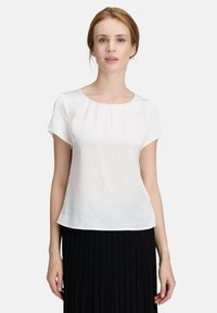 Weiße Kurzarmbluse mit Rundhalsausschnitt und sanften Falten an der Vorderseite; getragen mit einem schwarzen plissierten Rock. Glatte Textur.