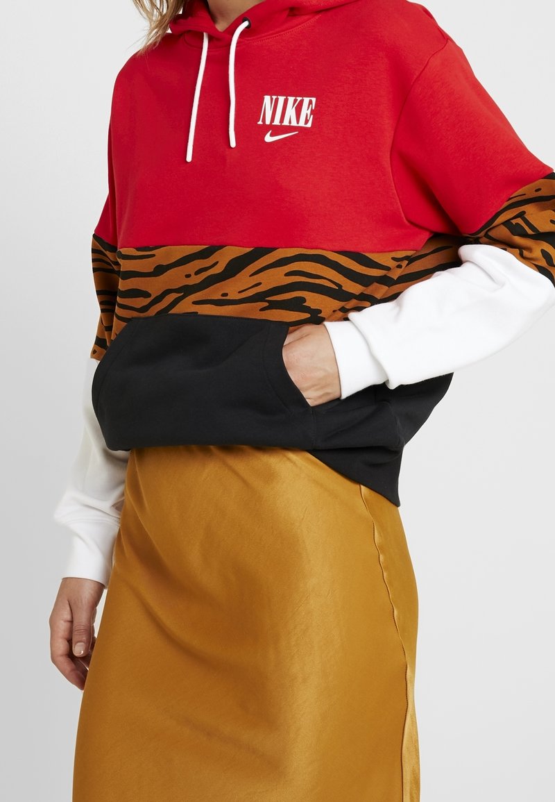 Punainen ja musta huppari, jossa on ruskea ja musta tiikeri-printti, valkoiset hihat. Sisältää etutaskun ja Nike-logon rinnassa.
