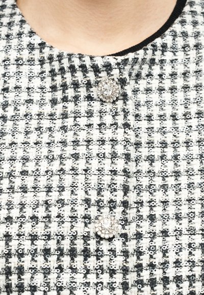 Veste en tweed noir et blanc avec des détails en sequins et deux boutons ronds en strass près du col.