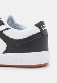 Svart och vit sneaker i läder och gummi, med en vit logotyp, en strukturerad svart panel och en vit gummisula.