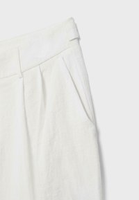 Pantalon en lin blanc à taille haute, passants de ceinture, plis à l'avant et poche latérale sur fond clair.