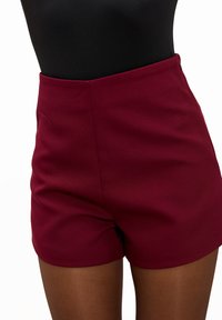 Shorts bordeaux en tissu doux, présentant une taille haute, des lignes épurées et aucun élément métallique ou ornement visible. Texture lisse sur toute la surface.