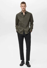 Oliivinvihreä napitetty paita sileästä kankaasta, säännöllinen mitoitus. Yhdistetty mustiin slim fit -housuihin ja mustiin nauhakengiin.