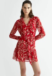 Red floral dress made of sheer fabric, featuring long sleeves, a V-neckline, ruffles along the front, and a tie belt at the waist.